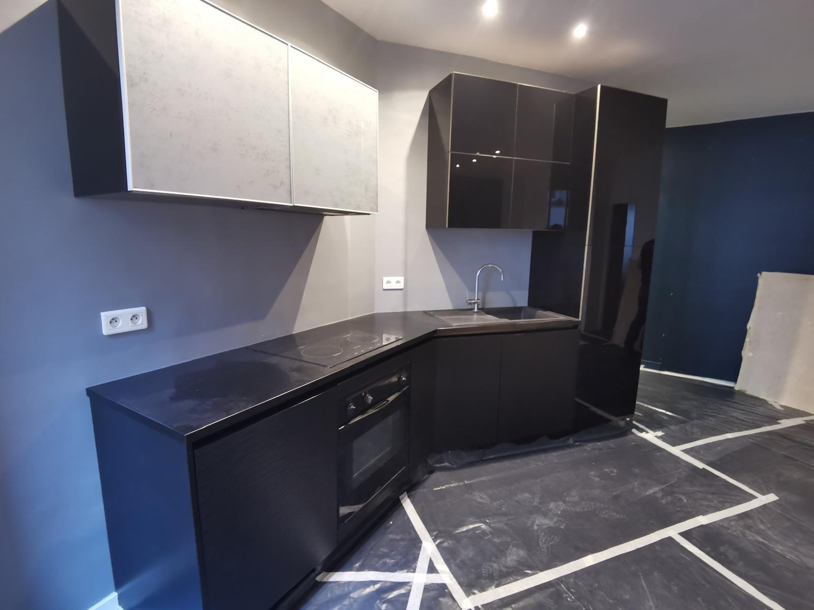 Cuisine moderne avec façades noires brillantes et placards hauts blancs mats en rénovation